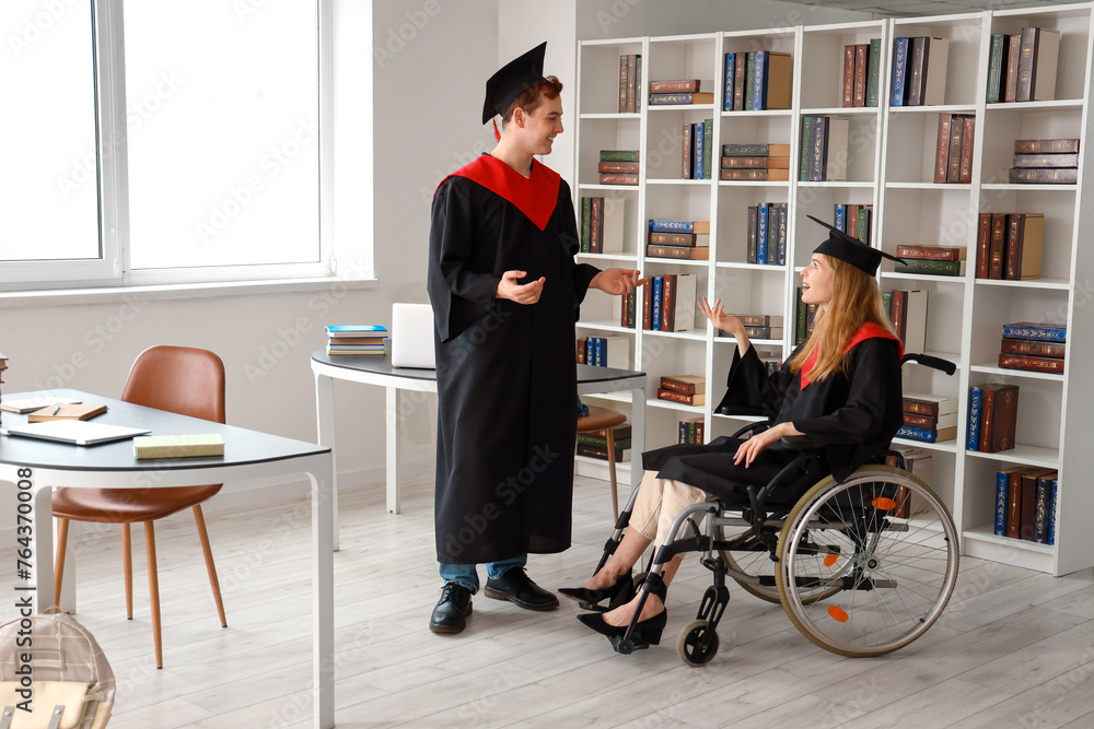 Female graduate in wheelchair chatting with classmate at university
