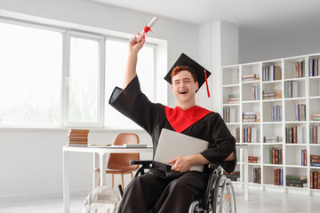 Canvas Print - Happy male graduate in wheelchair with laptop and diploma at university