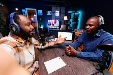 Content developer uses a smartphone selfie camera to create social media posts promoting an upcoming podcast with a guest. Black men having discussions and vlogging the radio program.