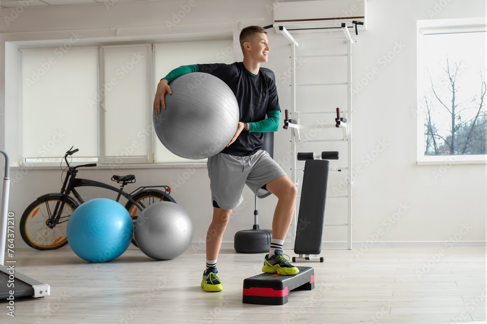 Sporty young man training with fitball on stepper at gym