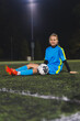 © PoppyPix - lovely girl in a blue uniform sitting on the grass with a ball and smiling at the camera. High quality photo