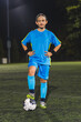 © PoppyPix - a young teenage girl wearing a blue uniform posing with a football ball in a stadium at night, active and sporty life. High quality photo