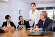 © JackF - Smart young woman sharing ideas in front of office colleagues of different ages taking notes at table with laptops