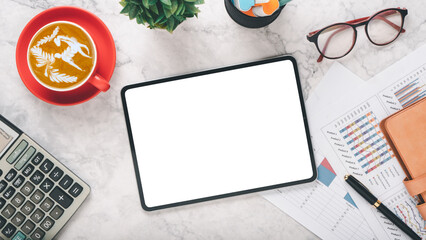 Wall Mural - A professional workspace scene featuring a blank tablet screen, a cup of latte art coffee in a red mug, glasses, and financial charts, all arranged on a marble surface.