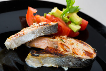 Wall Mural - Fried salmon steaks on black plate with sliced ripe tomatoes and avocado..