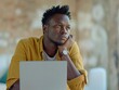 A mature, considerate young African freelance businessman is using a laptop computer while seated at a floor table, staring off into deep thought as he generates ideas and makes decisions.
