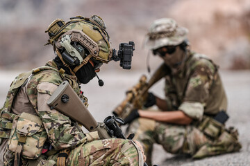 Soldiers in camo gear during a tactical operation with binoculars and rifles on a rocky terrain, showcasing military precision and readiness.