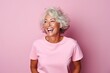Portrait of a happy senior woman with white hair laughing while standing against pink background