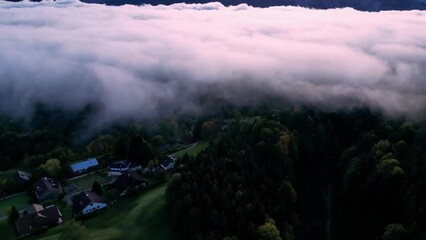 Wall Mural - Alpine village in the morning from above among the clouds. Cloudy sky with a town in the background