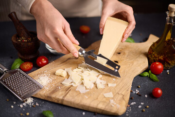 Wall Mural - Woman slicing Piece of Traditional Italian Parmesan Hard cheese into flakes on a wooden cutting board at domestic kitchen