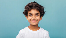 Closeup Portrait Of Amazing Cheerful Little Boy With Curly Hairdo In White T-shirt Looking At Camera With Happy Carefree Smile And Missed Milk Teeth. Indoor Studio Shot Isolated On Blue Background