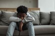 Depressed 15 years old African American teenager boy, sad and unhappy, sitting on the sofa.