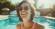 Lifestyle portrait of happy brunette woman wearing striped swimsuit, laughing and swimming in resort pool on holiday