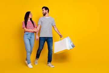 Canvas Print - Full size photo of cheerful man look at girlfriend hold shoppings bags go to empty space isolated on vibrant yellow color background