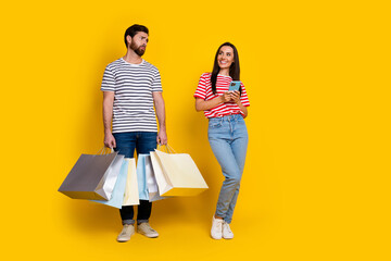 Wall Mural - Full size photo of upset guy look at positive girl dressed striped t-shirt jeans holding smartphone isolated on yellow color background