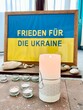 A sign reads in German: Peace for Ukraine. There are lit candles in the foreground. Concept: war and peace