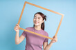 Young Asian woman holding photo frame on blue background