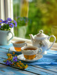 Morning tea session. Two cups of freshly brewed tea, accompanied by a white teapot, rest on a wooden table adorned with a blue cloth. Copy space