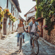 A couple is riding bikes along a bumpy cobblestone road, passing by old buildings and lush plants. The bicycle wheels are rolling smoothly on the rough terrain