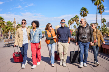 Wall Mural - Diverse smiling mature people celebrating leisure time on holidays. Group of positive middle-aged friends strolling carefree with their luggage down the street of a city carrying suitcase