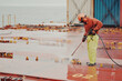 © I am from Mykolayiv - Seaman Seafarer In Safety Clothes Working On Deck Hatch Holding The Water Blasting Jet Machine. Corrosion Preventive Maintenance On Board The Ship