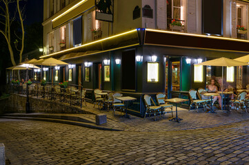 Wall Mural - Typical night view of cozy street with tables of cafe and easels of street painters in quarter Montmartre in Paris, France. Cityscape of Paris. Architecture and landmarks of Paris