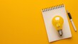 Light bulb, blank notebook and pen on yellow background with copy space, idea and creativity concept
