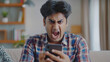 Angry Indian Guy Staring at Smartphone Screen with Frustration, Reacting to Bank Notification, Experiencing Scam, Fraud Alert, Screaming Over Battery Life, or Mobile App Crash with Intensity