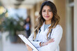 © romanets_v - A portrait of a young, confident Latina medical professional, wearing a white coat with a stethoscope, holding a clipboard, likely representing a doctor or a nurse in a clinical setting