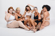 group of multi ethnic women of different ages in underwear sitting happy smiling, white background