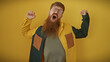 A bearded, yawning redhead man with eyeglasses in casual clothes over a yellow background portrays tiredness or boredom.