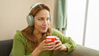 © Krakenimages.com - Attractive young hispanic woman enjoying coffee at home while listening to music with headphones.