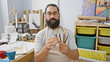 © Krakenimages.com - A bearded man examines paintbrushes in an art studio surrounded by paintings, canvases, and art supplies.