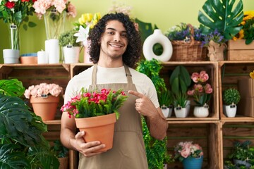 Poster - Hispanic man with curly hair working at florist shop holding plant smiling happy pointing with hand and finger