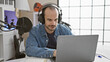 © Krakenimages.com - Hispanic man with beard and headphones working on laptop at music studio indoor.