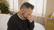 © Krakenimages.com - Mature hispanic man rubbing eyes with grey beard in indoor bedroom setting, showing emotions and stress.