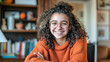 © Kowit - A young woman with curly hair is smiling and wearing glasses. She is sitting at a desk with a chair and a lamp
