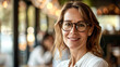 © Kowit - A woman wearing glasses is smiling and posing for a picture. She is wearing a white shirt and she is in a restaurant