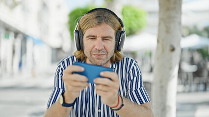 Sticker - A middle-aged man with headphones uses a smartphone on a sunny city street, evoking a modern, urban lifestyle.