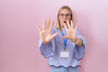 Sticker - Young caucasian business woman wearing id card afraid and terrified with fear expression stop gesture with hands, shouting in shock. panic concept.