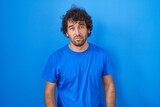 Fototapeta  - Hispanic young man standing over blue background looking sleepy and tired, exhausted for fatigue and hangover, lazy eyes in the morning.