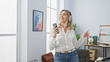© Krakenimages.com - A joyful middle-aged woman enjoys music on headphones while holding a smartphone in a modern office.