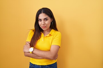 Wall Mural - Young arab woman standing over yellow background happy face smiling with crossed arms looking at the camera. positive person.