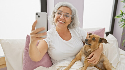 Poster - A grey-haired woman takes a selfie with her dog in a bright bedroom setting