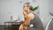 © Krakenimages.com - Mature hispanic woman with grey hair and glasses, pondering in a modern indoor setting.