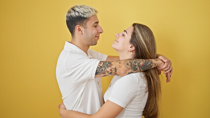 Wall Mural - Beautiful couple smiling confident hugging and looking each other over isolated yellow background