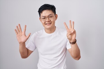 Sticker - Young asian man standing over white background showing and pointing up with fingers number eight while smiling confident and happy.