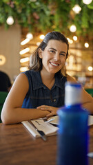 Poster - Young beautiful hispanic woman smiling happy sitting on the table at the restaurant