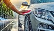 Close up of hand washing a car with water hose in driveway during summer day