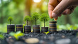 A hand places a coin on stacked coins with miniature trees sprouting, representing financial growth and eco-investment concept.